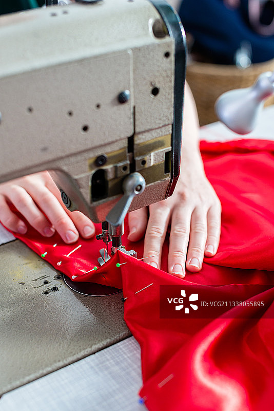 女人用手缝缝纫机，添加纽扣，红色织物，固定大头针图片素材
