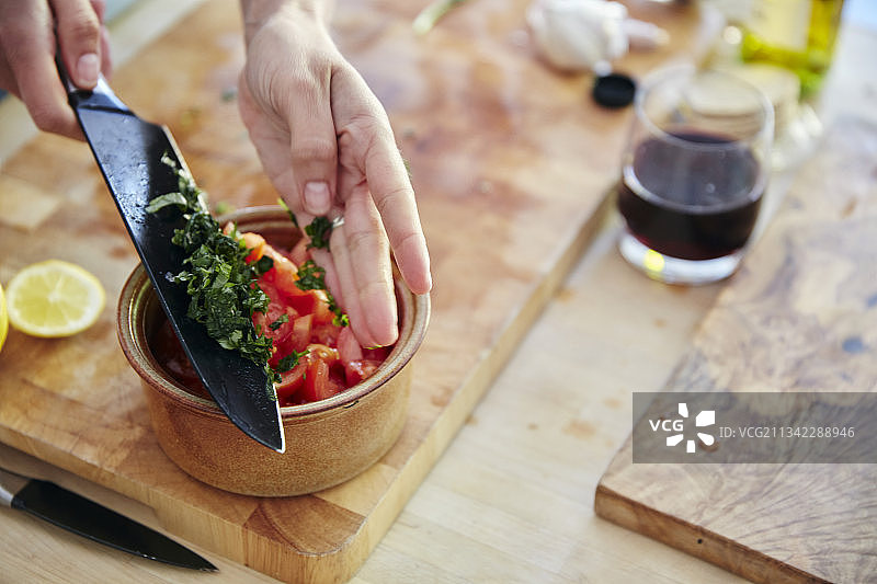 英国，家庭健康烹饪，切碎的罗勒被添加到番茄沙拉中图片素材