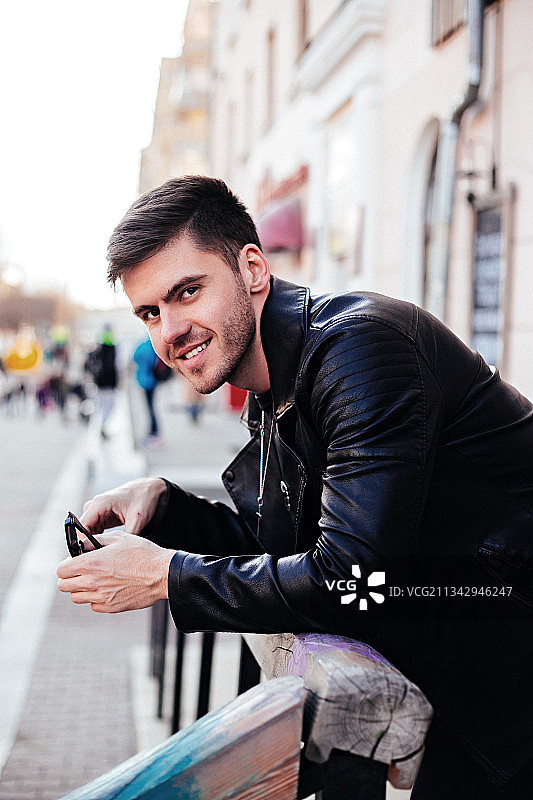 一名微笑的年轻人站在城市里使用手机图片素材