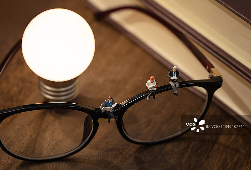 微缩创意书本木桌上发光的灯泡眼镜上阅读的人图片素材