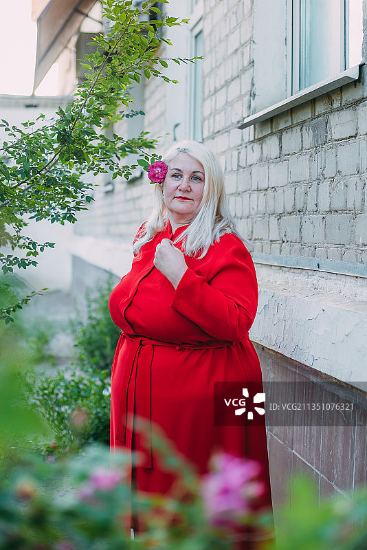 哈萨克斯坦，一名身穿红色连衣裙的女子站在户外的花园里图片素材