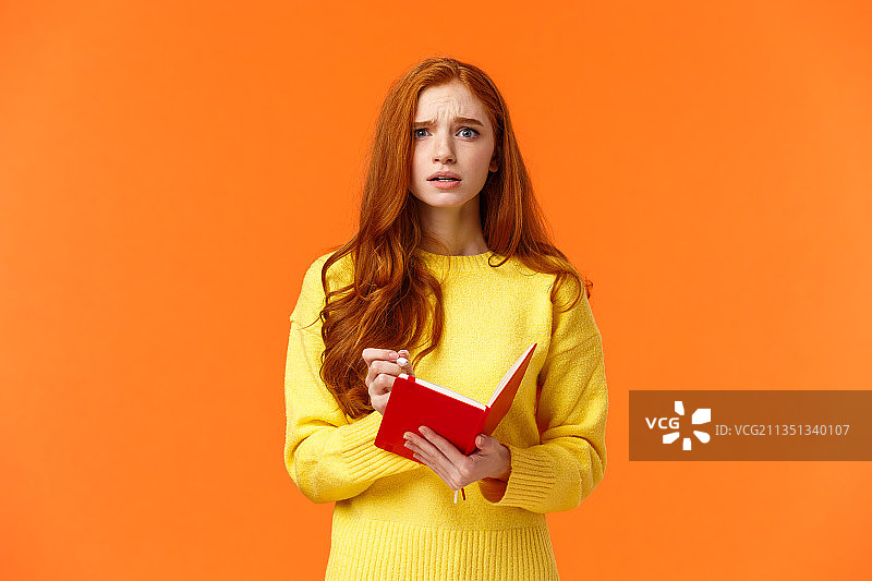 年轻女子手持一本书，站在橙色背景下图片素材