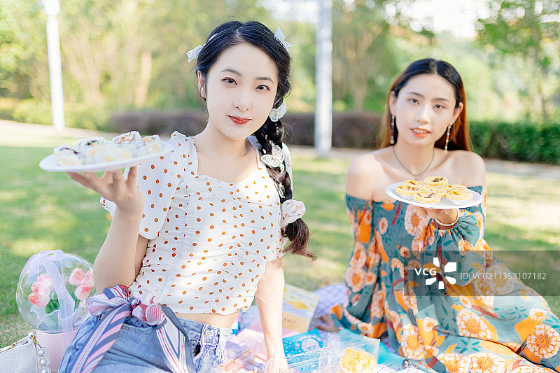 两个亚洲青年美女闺蜜在户外野餐垫上野餐拿着寿司和披萨图片素材