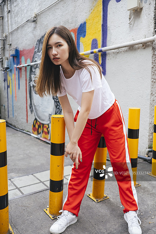 时尚肖像-年轻的亚洲泰国妇女在白色衬衫和红色运动裤在黄色屏障在街道小巷。图片素材