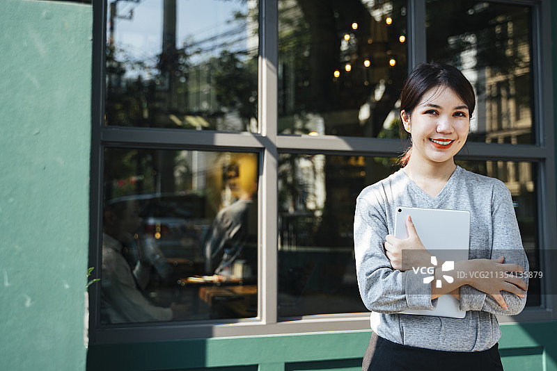 优雅的年轻女商人手持平板电脑在咖啡馆背景。图片素材