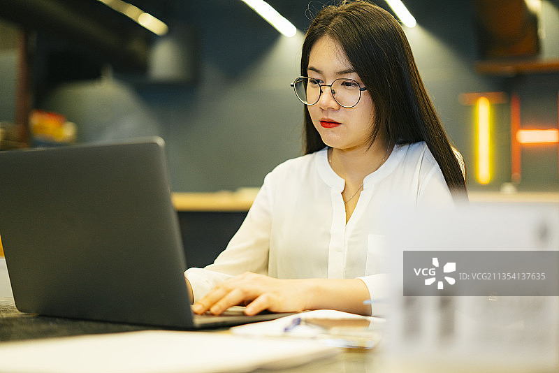 美丽的亚洲办公室女性戴着眼镜工作在办公室的笔记本电脑。图片素材