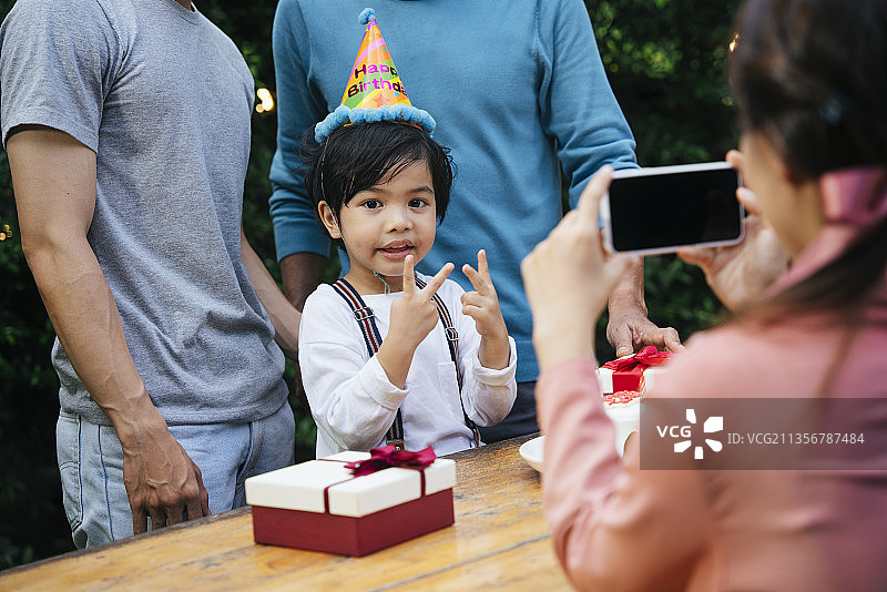 亚洲小孩和家人在户外庆祝生日。妈妈用智能手机拍照。图片素材