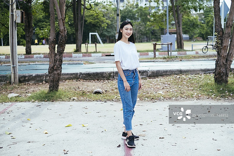 泰国亚洲妇女全身肖像穿着白衬衫和牛仔裤裤子站在公园的街道上。图片素材