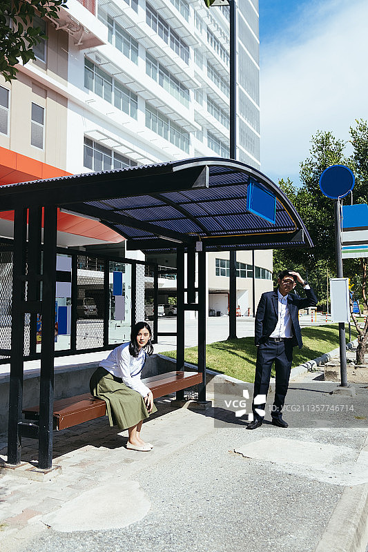 一男一女坐在公车站等公车到他们的办公室。图片素材