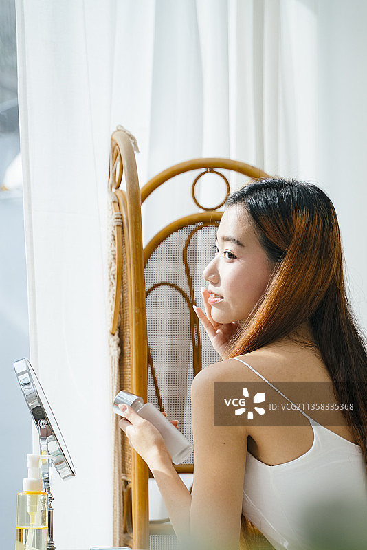 侧视图-年轻的亚洲妇女在窗户附近做化妆在家里。自然光线。图片素材