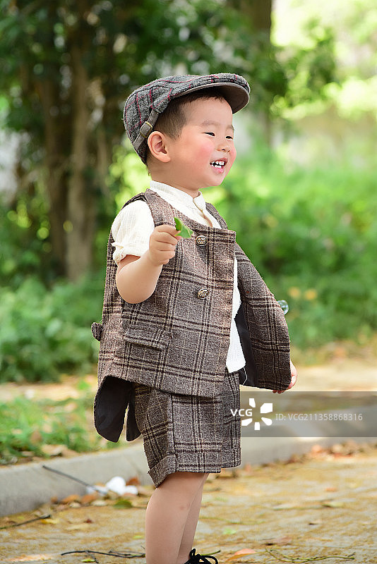 阳光下林荫小路上穿着短袖西服手拿树叶玩耍的小男孩图片素材