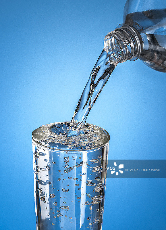 水倒在一个杯子，水倒在蓝色背景的瓶子的特写镜头图片素材