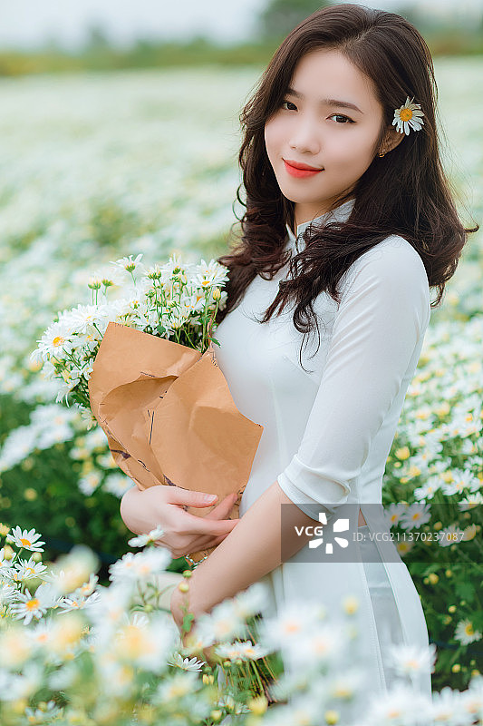 美丽的女孩在黛西的田野，美丽的女人的肖像握着花束，而站在田野上，越南图片素材