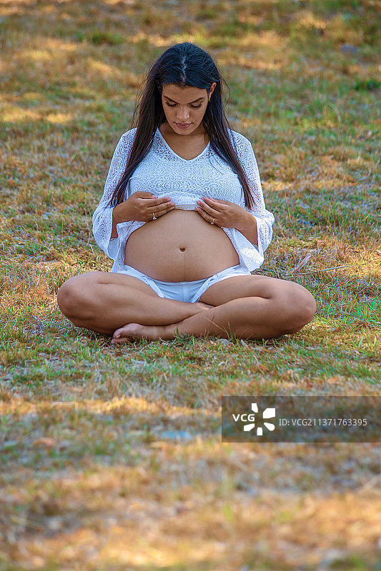 孕妇，古巴，圣克拉拉，孕妇坐在草地上，全身触摸腹部图片素材