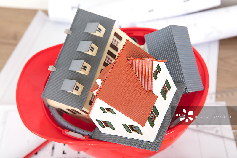 倒放的红色安全帽和帽子里塞满的小房子模型图片素材