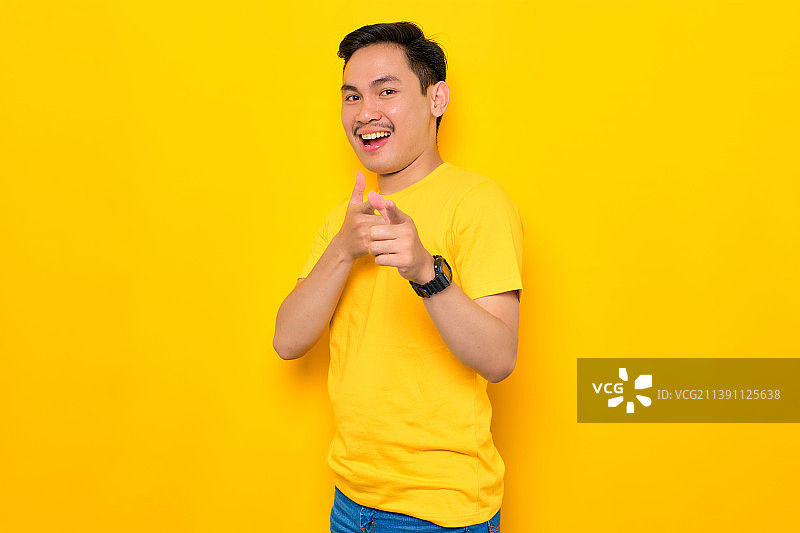 微笑的亚洲年轻男子指着相机孤立的黄色背景，印度尼西亚图片素材