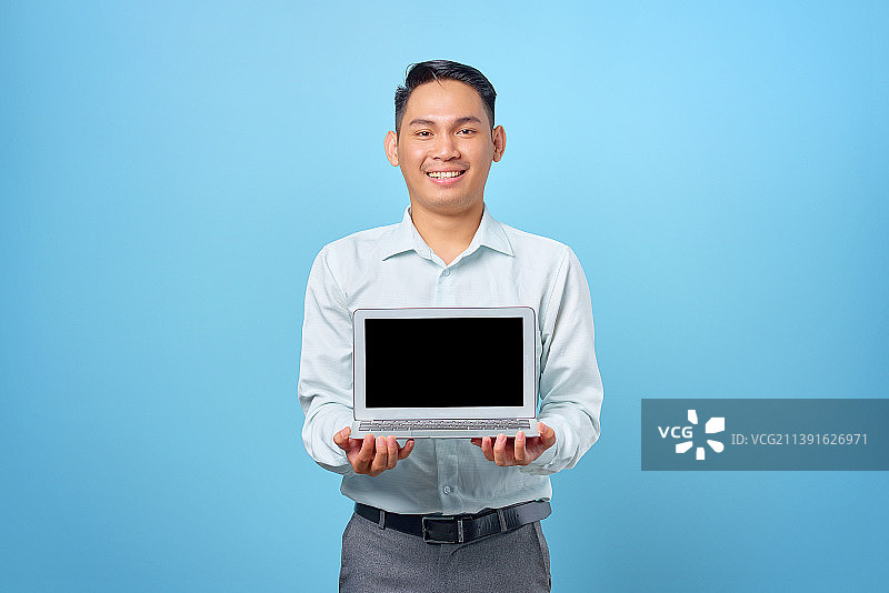 印度尼西亚，微笑的年轻英俊的商人展示着蓝色背景的黑屏笔记本电脑图片素材