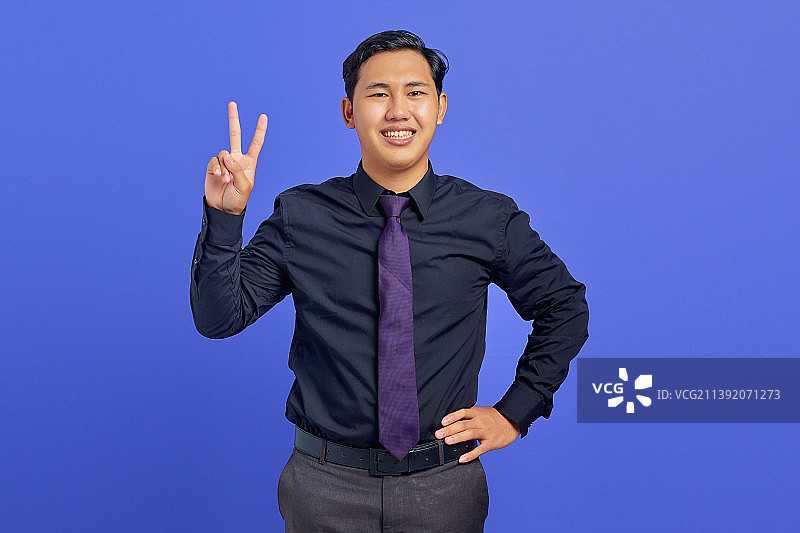 英俊开朗的亚洲青年在紫色背景上展示和平标志，印度尼西亚图片素材