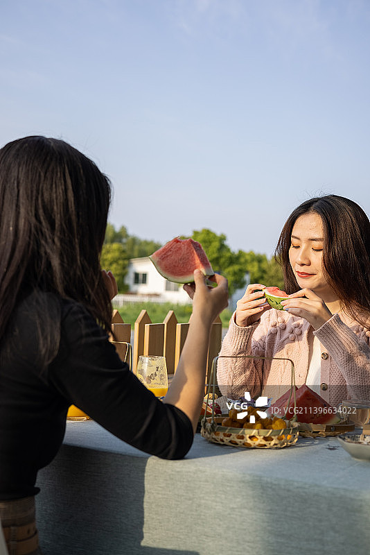 春季夕阳下两个年轻女孩社交聚会喝下午茶吃西瓜聊天图片素材