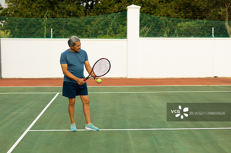 全貌双种族老年男子手持球拍和球在网球场打网球图片素材