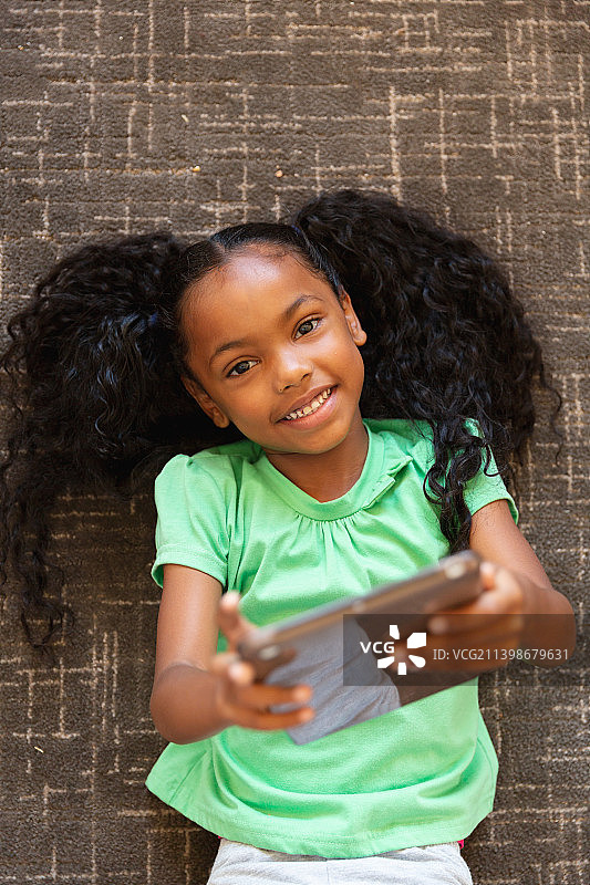 非洲裔美国小学女孩的头顶肖像与数码平板躺在学校的地毯上图片素材