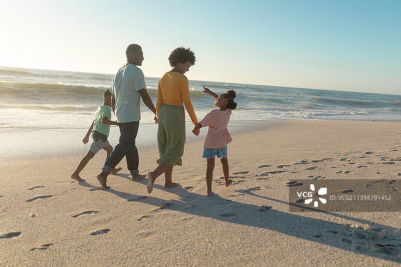 阳光灿烂的日子，非裔美国父母牵着孩子在海滩上散步图片素材