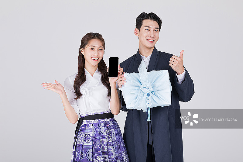 一对20岁的韩国夫妇，身穿现代韩服，手持传统盒子和智能手机图片素材
