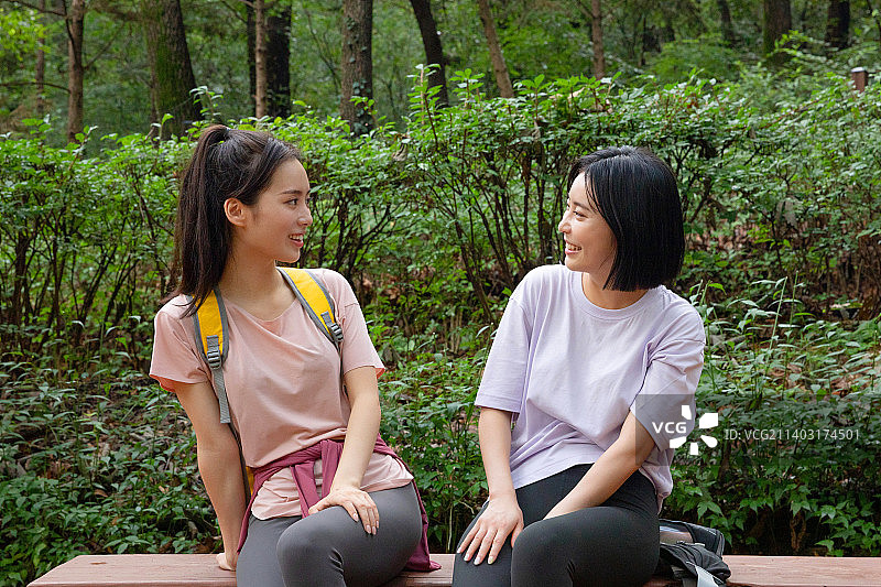 两个20多岁的韩国亚裔女性朋友在山上徒步和登山，以此来休息图片素材