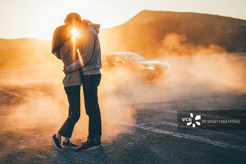 日落时，一对情侣站在路上对着天空接吻图片素材