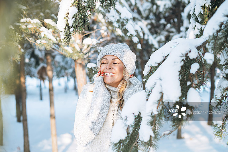 在俄罗斯斯维尔德洛夫斯克州叶卡捷琳堡下雪的冬季森林里，身穿冬装微笑的金发女子双手贴着脸图片素材