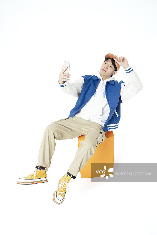 坐在橙色凳木箱子上玩手机的年轻男生图片素材