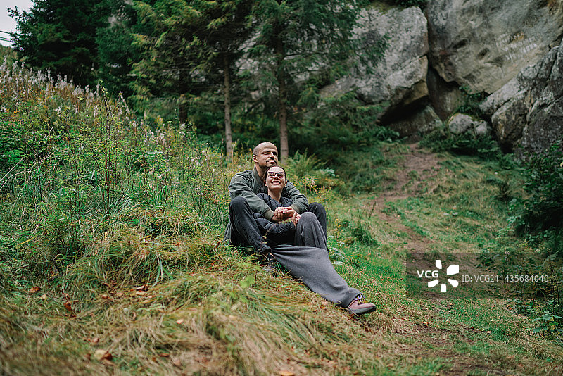 西班牙，一对幸福的夫妇微笑着坐在草地上，映衬着森林风景图片素材