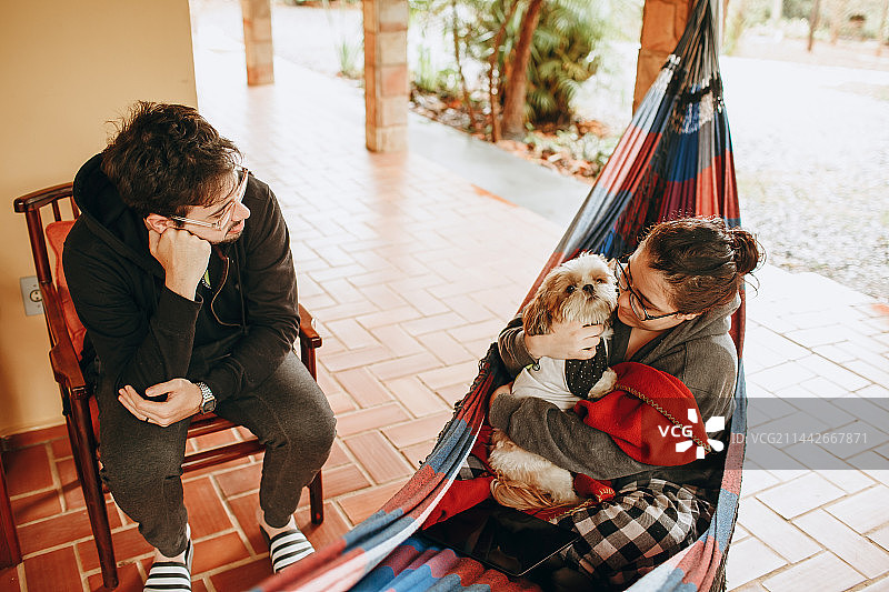 巴西米纳斯吉拉斯州贝洛奥里藏特，一对夫妇和一只小哈巴狗在家里的吊床上休息图片素材