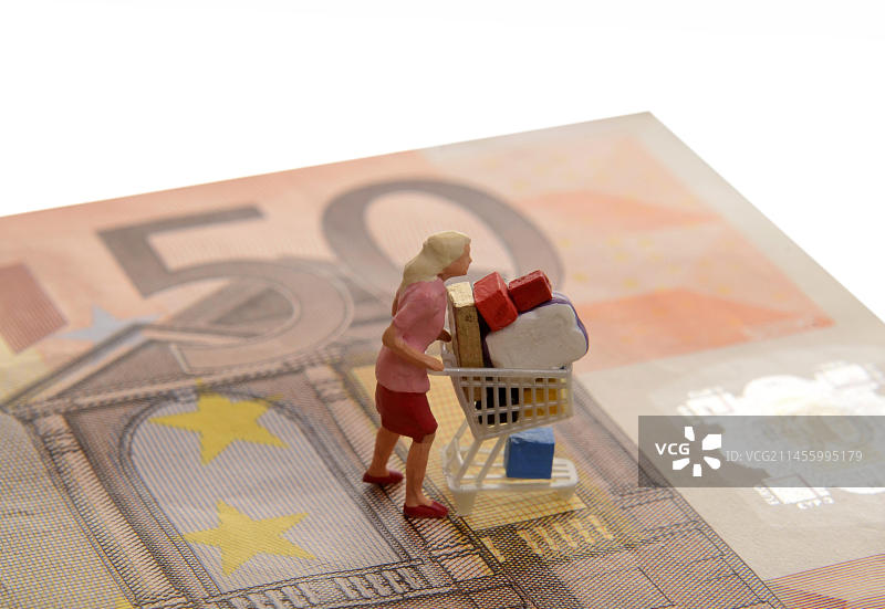 50欧元纸币上的微型女性形象推着满车的购物车，象征着购物狂图片素材