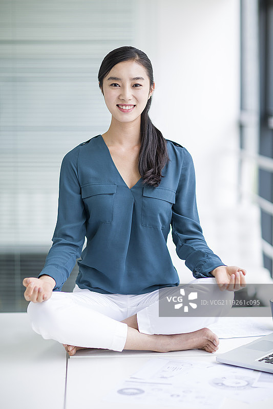 年轻商务女士坐在办公桌上练习瑜伽图片素材