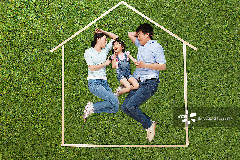 幸福的一家三口躺在草地上的模型房子里图片素材