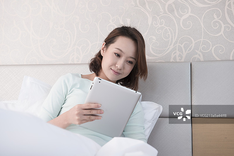 Young woman using digital tablet in bed图片素材