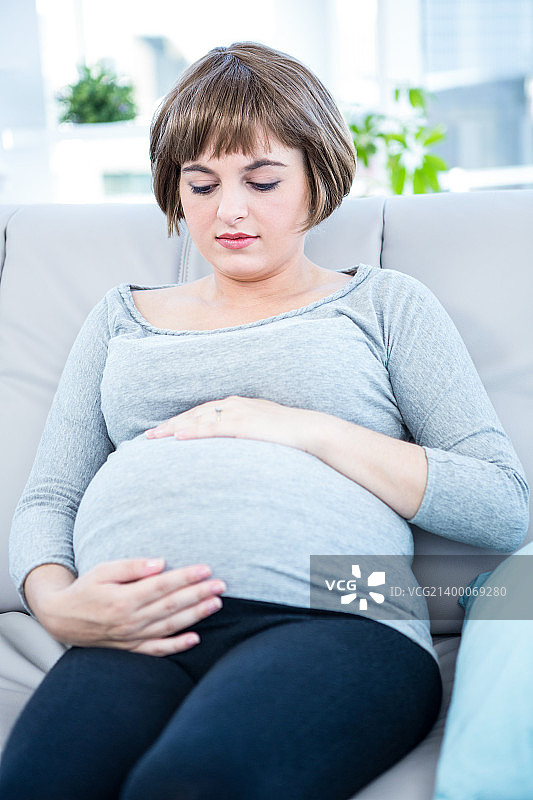 一名孕妇坐在家里的沙发上，摸着自己的肚子图片素材