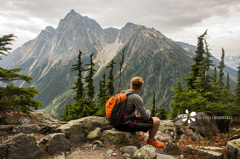 一位徒步旅行者坐在加拿大不列颠哥伦比亚省麦克唐纳山前。图片素材