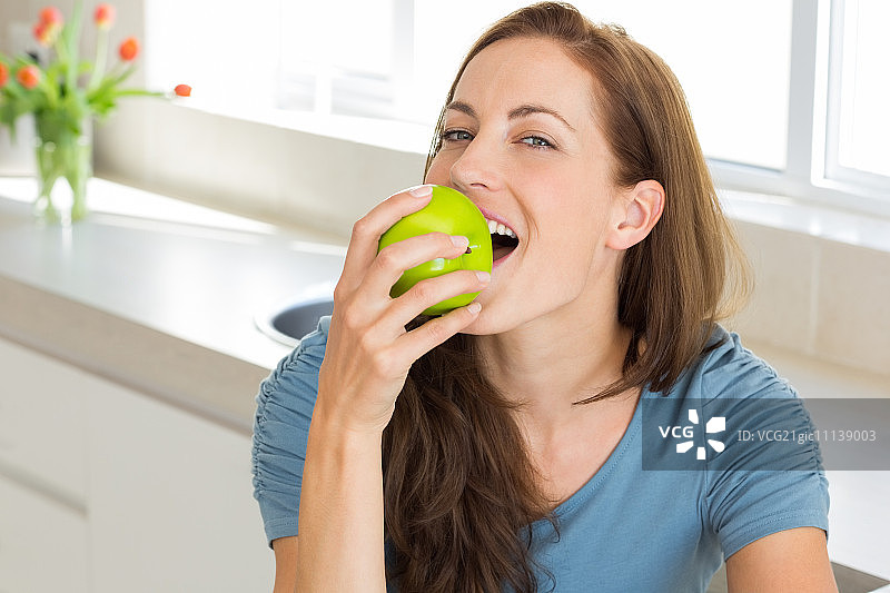 一个微笑的年轻女子在厨房吃苹果的特写图片素材