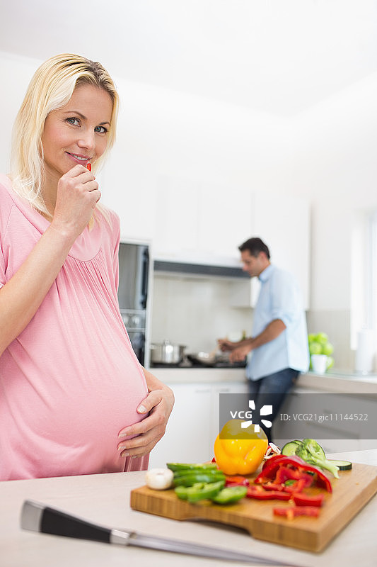 怀孕微笑的女人和切碎的蔬菜和男人在厨房做饭的房子图片素材