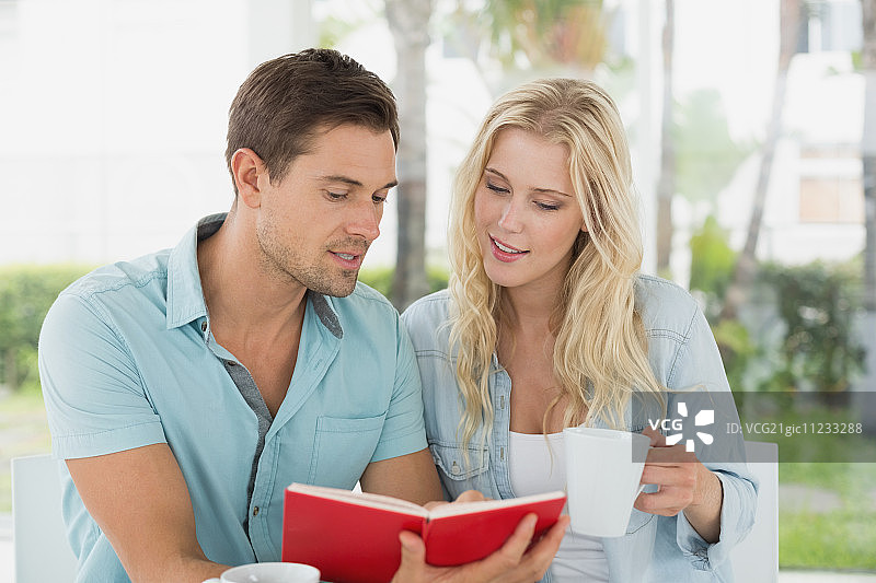 在阳光明媚的日子里，一对时髦的年轻夫妇在咖啡馆的露台上一起喝咖啡看书图片素材