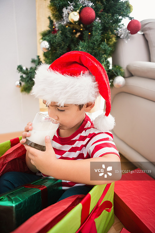 可爱的男孩在大圣诞礼物喝牛奶在家里的客厅图片素材