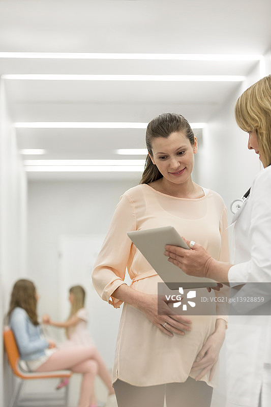 医生在诊所走廊用平板电脑与孕妇交谈图片素材