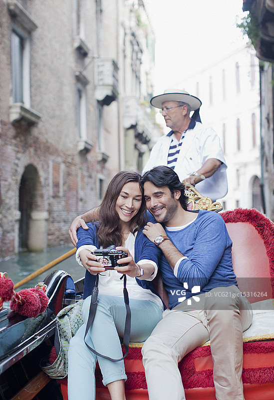 一对微笑的夫妇在威尼斯运河的贡多拉上用数码相机自拍图片素材
