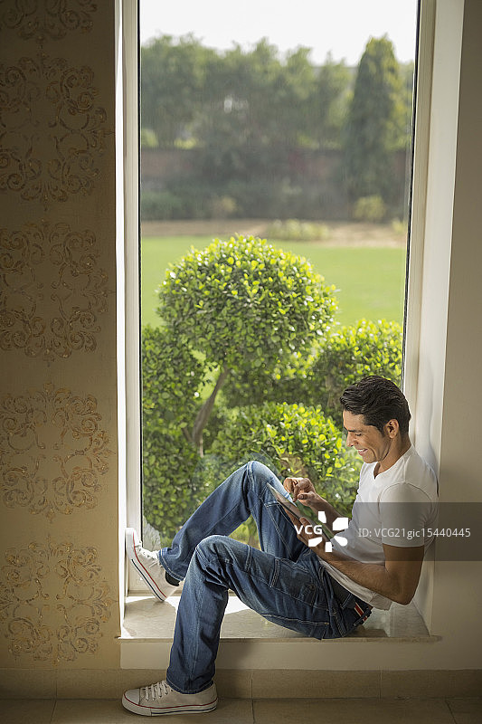 印度，一名男子坐在窗台上使用数码平板电脑图片素材