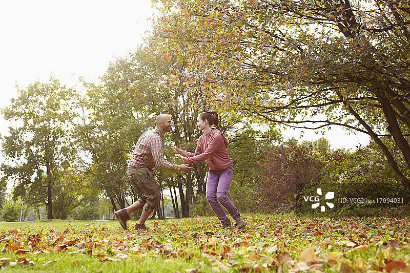 秋天的一天，一对相爱的年轻夫妇在公园里玩捉迷藏，背光下。图片素材