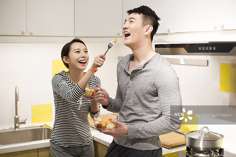 快乐的年轻情侣在厨房吃水果沙拉图片素材