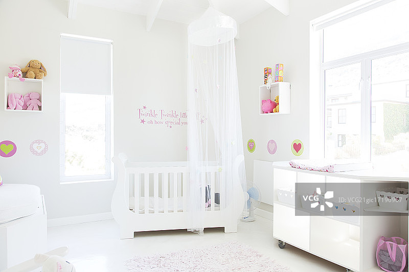 色彩柔和的婴儿房里，有薄纱顶棚的白色婴儿床图片素材