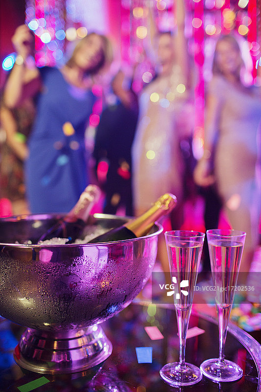冰桶里的香槟酒瓶和夜店里的香槟笛子，人们在背景中跳舞图片素材